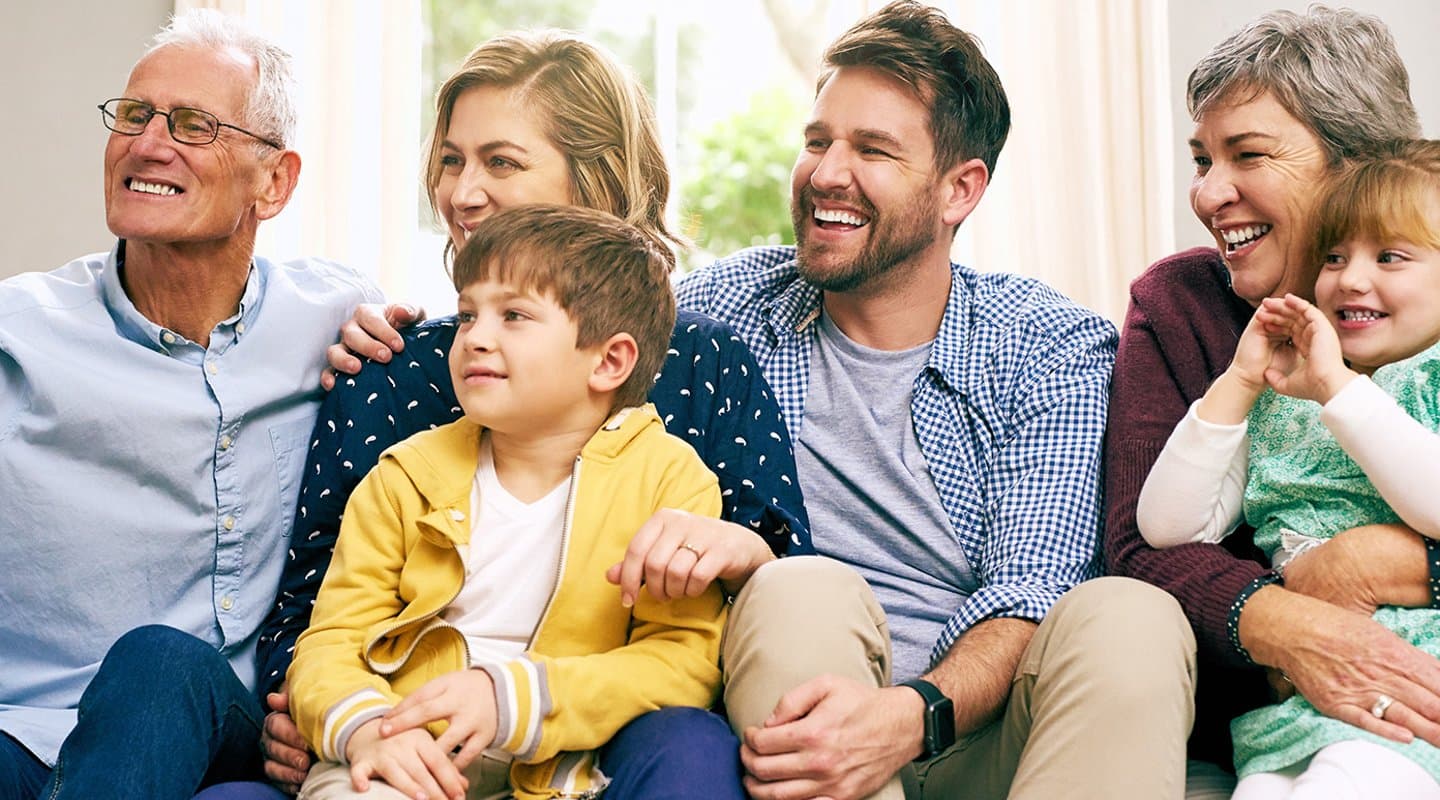 a multigenerational family sits on a couch and smiles for a picture