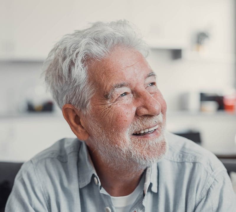 Close up photo of an older man with white hair and a white beard smiling.