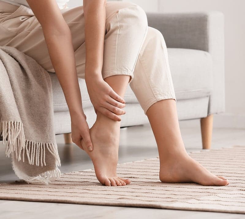 A woman rubs leg while sitting on a couch