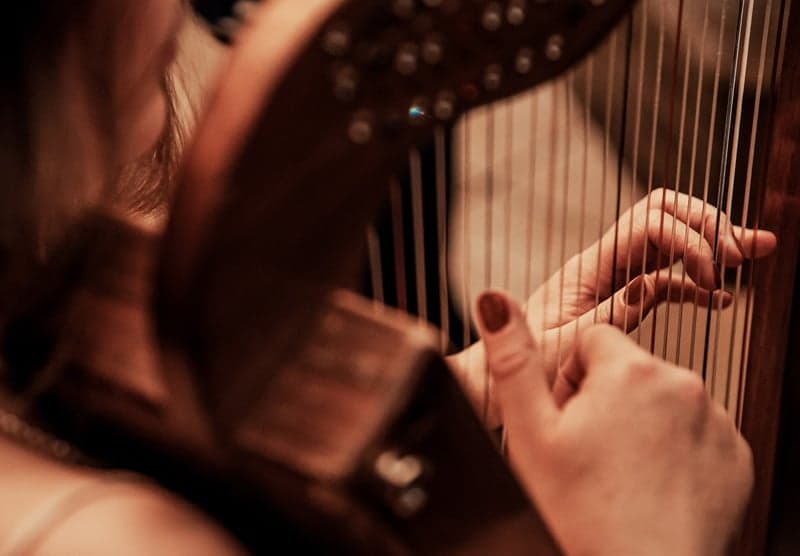 Looking over the shoulder of a harp player plucking harp strings