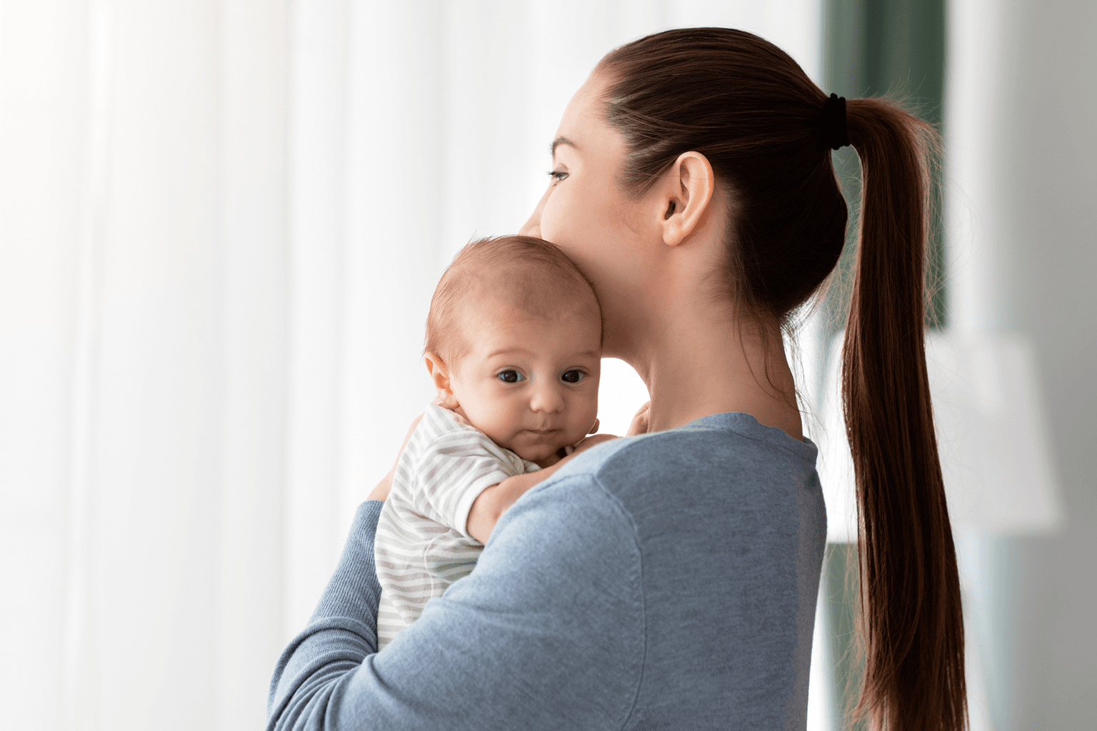 Young Woman Holding Cute Little Newborn Baby Standing Near Window