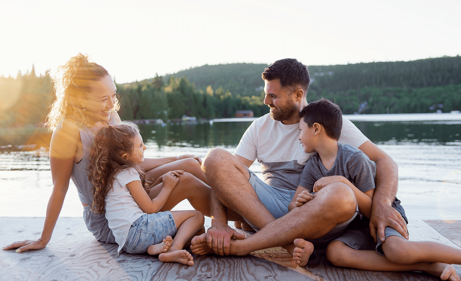 parents with two elementary aged kids sitting on dock at lake and smiling