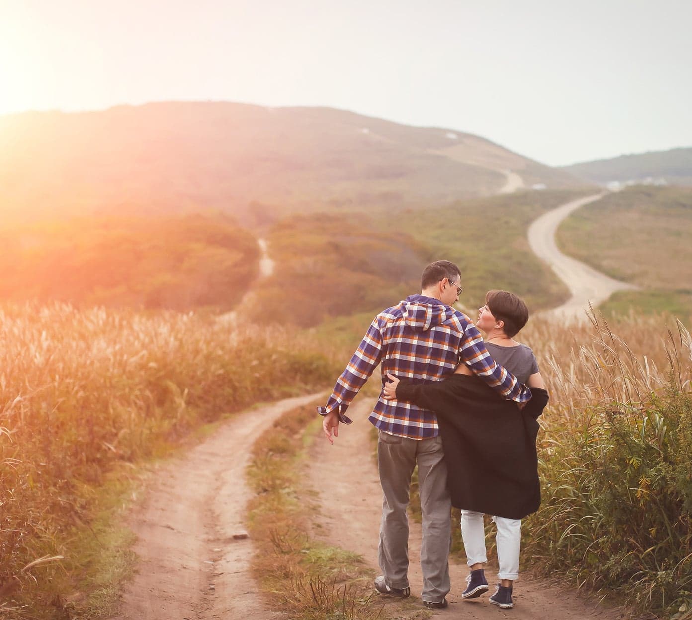 A man and a woman walk on a dirt road while the sun rises